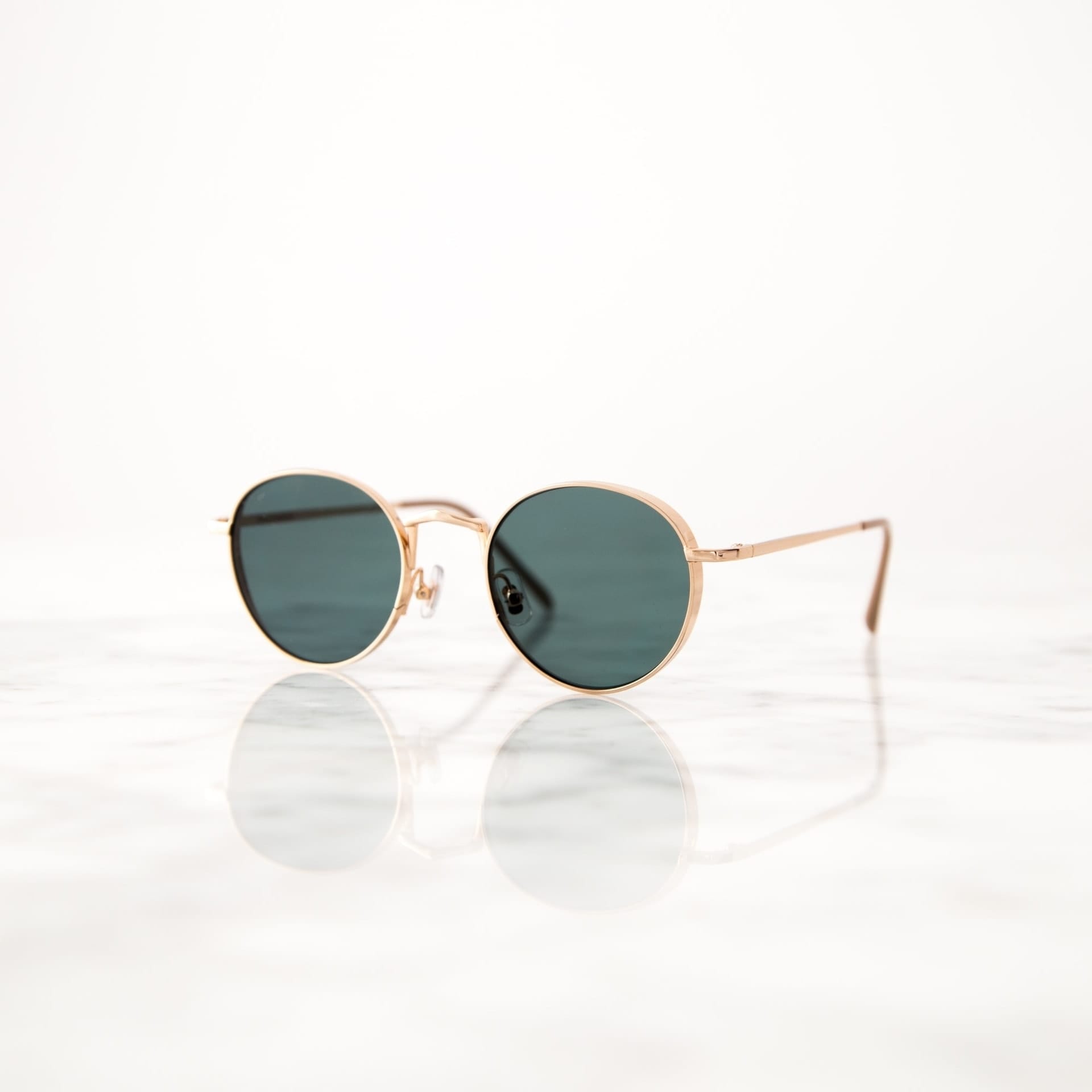 Sonnenbrille mit goldenem Gestell auf reflektierendem Marmoruntergrund